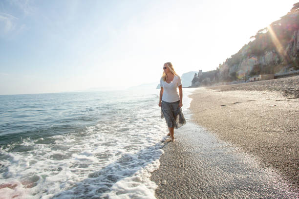 istock Woman walks along surf edge on deserted  beach 1320499562