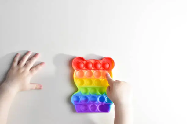 Photo of Children's hands play with the rainbow pop it fidget toy. Touch bear shaped toy is a reusable silicone stress relief toy. Anti-stress therapy