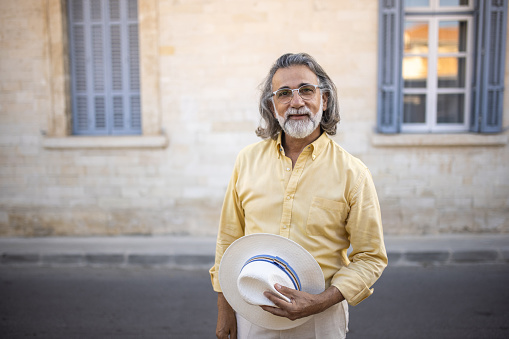 Portrait of elegant senior man with long gray hair and beard, at city during his vacation, he's standing and looking at camera