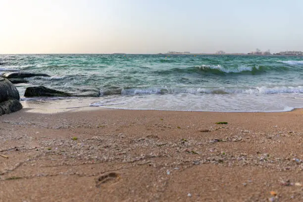 Waves crashing against the shore of Persian Gulf, seascape seen from Dubai Bluewaters Island, Dubai coast in the background, sandy beach.