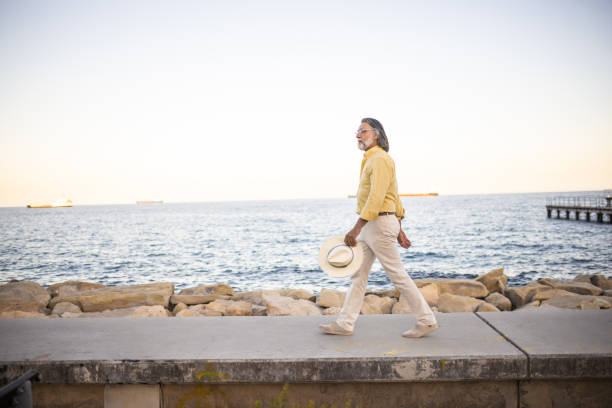 Side view of well-dressed mature male tourist walking at waterfront and enjoying the view