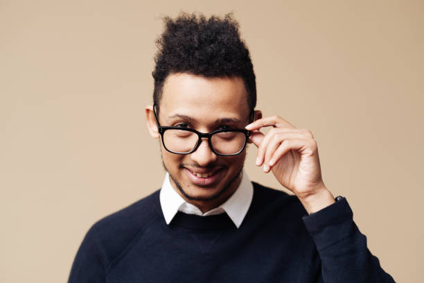 istock Afro Good looking guy in black sweater and glasses posing on beige background 1320504373