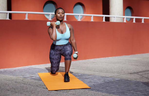 Shot of a young woman on a gym mat using dummbells against an urban background Your only worthy competitor is YOU lunge stock pictures, royalty-free photos & images
