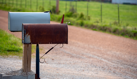 senior man putting letter in antique Irish mailbox, metal mailbox with rust, man in yellow vest. vertical image.
