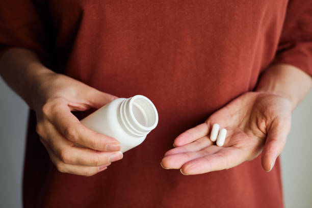A woman pours pills or vitamins from a jar onto her hand. Taking vitamins or medications. The concept of health care, medicine, pharmacies, disease prevention. A jar with pills or vitamins in the hand stock photo
