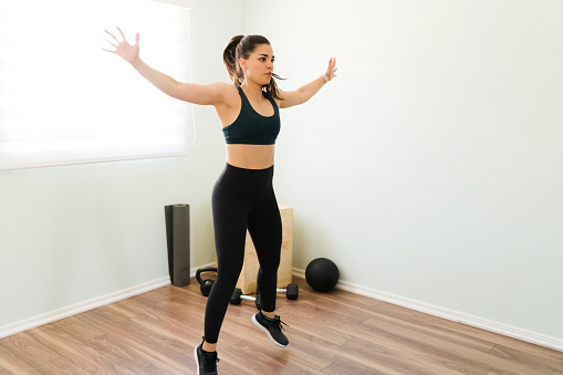 Healthy woman with black sporty clothing working out with jumping jacks and sweating during her daily cardio exercises at home