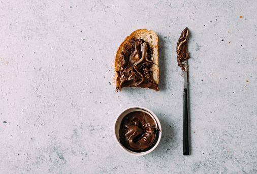 Morning rituals: Piece of homemade bread and knife covered in cocoahazelnuts spread, lying on a marble background