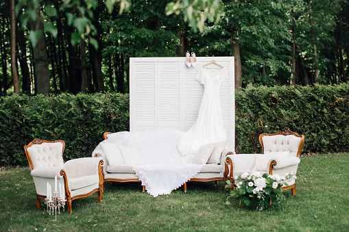 Morning of bride, gathering bride in nature, photo zone. Furniture, screen, flowers, wedding dress and shoes. Eco style wedding.