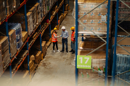 Supervisor shaking hands with one of employees in warehouse during inventory