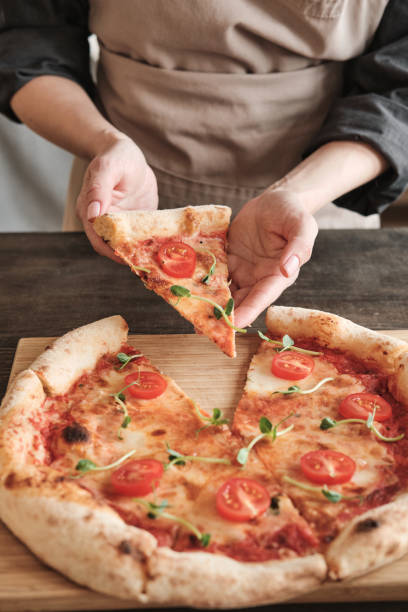 istock Female hands taking hot pizza slice with tomato and pea leaves while eating it after baking 1320527765