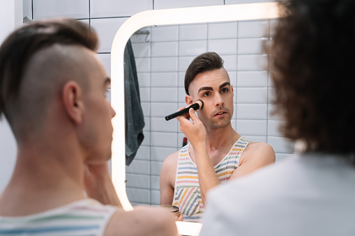 Gay friends are doing make-up together in the bathroom looking in the mirror. Gender Diversity Concept