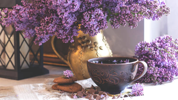 istock Decorative composition with a Bouquet of lilacs in a light kitchen interior. Clay cup of tea and chocolate cake. A bouquet of lilacs in a vase. Spring floral background with lilacs. Aesthetics 1320530889