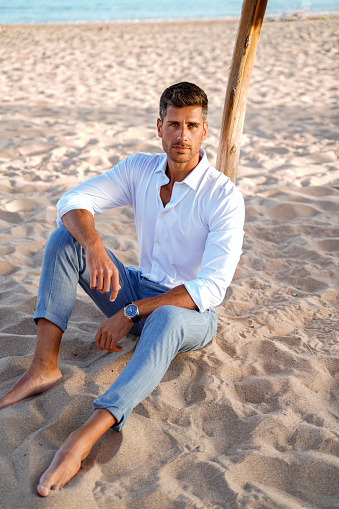 Recreational entrepreneur. Handsome man relaxing on the sandy beach, wearing elegant fashionable clothes.