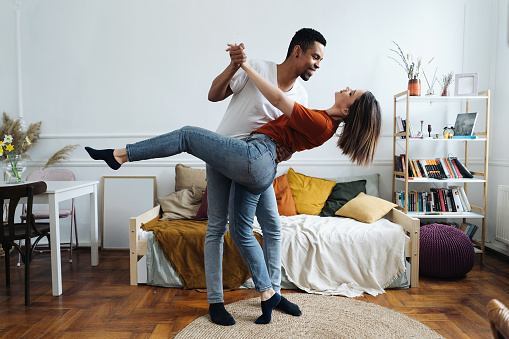 Cheerful active romantic african caucasian couple dancing in bedroom together, happy carefree young black husband and white wife enjoy weekend morning laughing bonding having fun at home