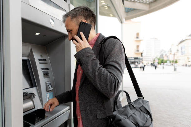 istock Businessman using card at an ATM talking on phone 1320543823