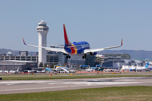 Portland, Oregon, USA - April 15, 2021: A Southwest Airlines 737 comes in for landing on runway 28R at Portland International Airport. In the background is the control tower and terminal with the new concourse E extension visible.