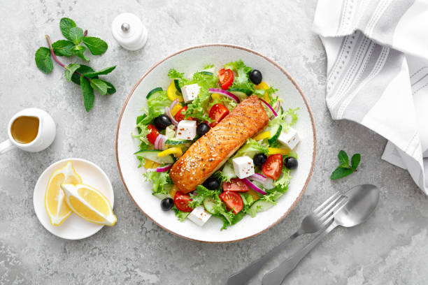 Salmon fish salad. Fresh vegetable greek salad with tomato, pepper, lettuce, olives, cucumbers, feta cheese and grilled salmon fish fillet in bowl, healthy food, omega 3, keto diet, mediterranean cusine, top view. ensalada de pescado de salmón. ensalada griega de verduras frescas con tomate, pimiento, lechuga, aceitunas, pepinos, queso feta y filete de pescado de salmón a la parrilla en tazón, comida saludable, omega 3, dieta cetogénica, cusine mediterráneo, vi