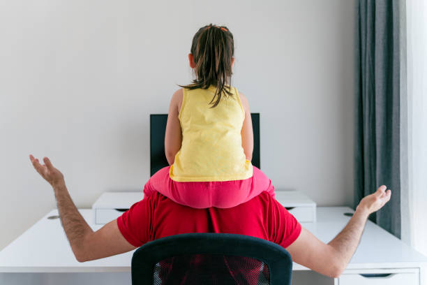 junger vater hält an den schultern seine kleine tochter versucht, am computer zu hause zu arbeiten - child office chaos computer monitor stock-fotos und bilder