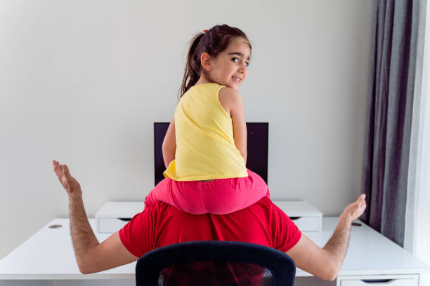 junger vater hält an den schultern seine kleine tochter versucht, am computer zu hause zu arbeiten - child office chaos computer monitor stock-fotos und bilder