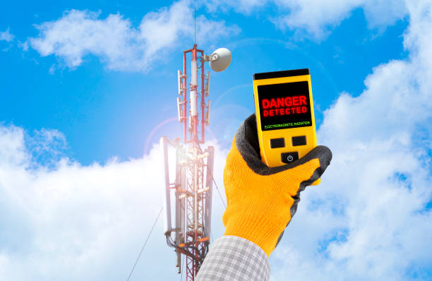 Measuring electromagnetic radiation from a cell tower. The device indicates hazardous radiation with text Danger. Influence of the electromagnetic field on humans concept.