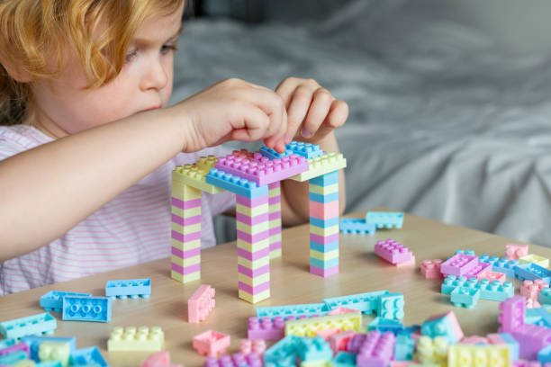 テーブルに座って、カラフルなおもちゃのビルディングブロックで遊んで小さなかわ�いい未就学児の女の子。 - fine motor skills ストックフォトと画像