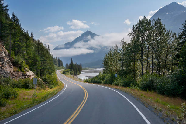 camper viaggia lungo un'autostrada curva in alaska sotto le montagne vicino a seward in un pomeriggio soleggiato - road foto e immagini stock