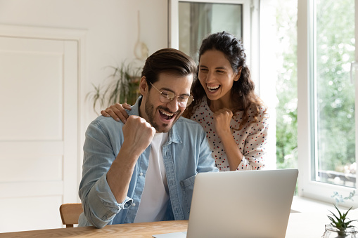 Overjoyed loving young bonding family couple looking at computer screen, getting email with amazing good news, celebrating online lottery betting gambling giveaway win, internet success concept.