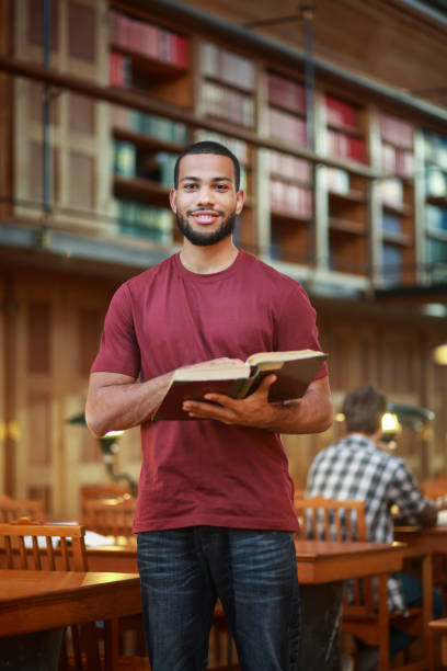 istock Young man reading a book in public library 1320557943
