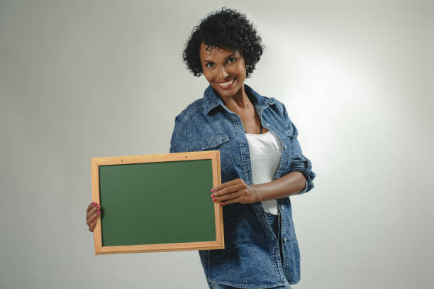 istock Happy black young woman holding empty board to write on 1320585835