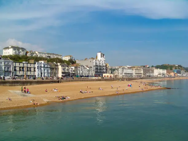 A view of the sunny beach with the town line and some beachgoers relaxing by the emerald sea