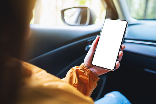 Mockup image of a woman holding and using mobile phone with blank screen in the car