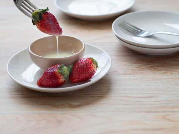 This is a scene where a strawberry is stuck on a fork and dipped into condensed milk in a cup.