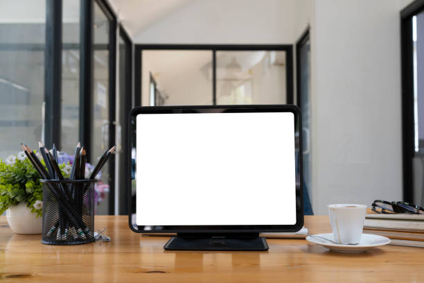 istock Front view computer tablet with white screen, pencil holder and coffee cup on wooden table. 1320602297