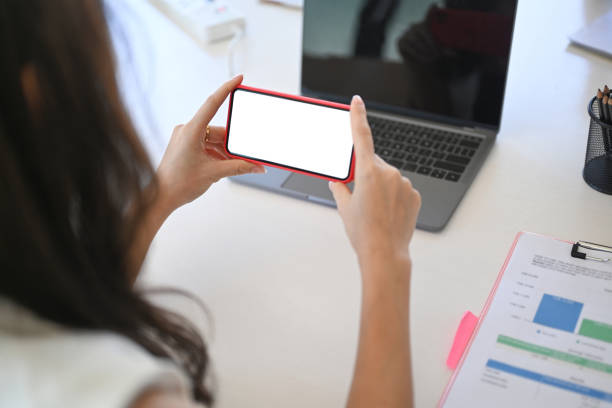 istock View over businesswoman holding horizontal mobile phone while sitting in office. 1320602303