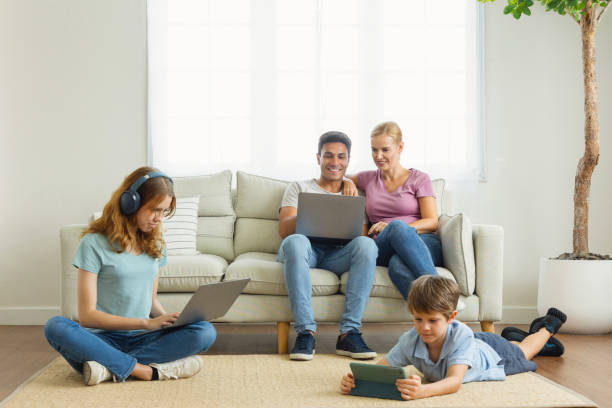 work from home. A parent using a laptop on the couch in the living room. Children use the phone app, search for information, using wifi 5G internet. Family ignore and gadget addiction concept stock photo