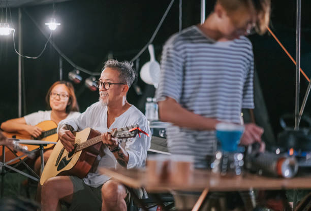 asian chinese senior man playing guitar enjoying time with family and friends at garden party gathering camping tent at night asian chinese senior man playing guitar enjoying time with family and friends at garden party gathering camping tent at night father and son guitar stock pictures, royalty-free photos & images