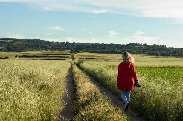 カメラを手にフィールドの間の道路を歩く認識できない写真家 - footpath single lane road road farm ストックフォトと画像