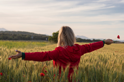 woman in unrecognizable red jacket with open arms in a cultivated field. Enjoying freedom