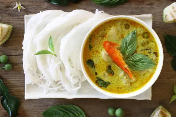 Photo of Top view of green curry fish ball served with Thai rice vermicelli in white plate on wood table, look delicious.