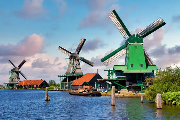 ZAANSE SCHANS, NETHERLANDS - CIRCA AUGUST 2020: Dutch windmill in green countryside close to Amsterdam, with blue sky and river water.