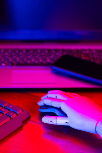 istock Creative freelancer workplace in neon light. Artificial hand on the keyboard. Place for digital artist to work with laptop, monitor and smartphone. Concept of work at home 1320631550