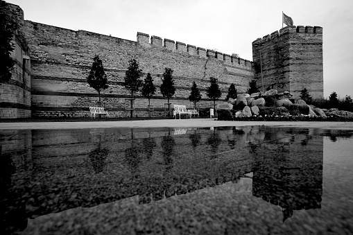 Part of historical Byzantine wall In Istanbul. The historical Byzantine wall and a tree is towards the blue sky. there is reflection of the wall and tree in the puddle.