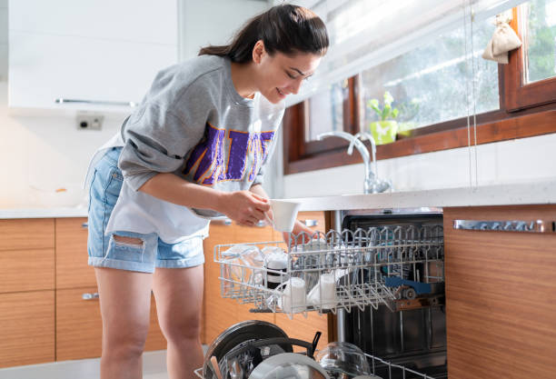 istock Young woman is putting dishes into dishwasher in kitchen. 1320637765