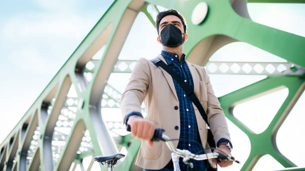 istock Low angle view of young business man commuter with bicycle going to work outdoors on bridge in city, coronavirus concept. 1320637935