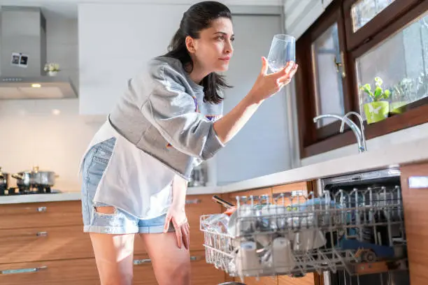 Photo of Young woman takes a glass out of the dishwasher in kitchen.