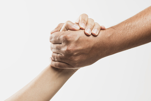 Two unrecognizable caucasian peoples hands are holding each others wrist in front of pure white background. Arms are forming a diagonal line from the right upper corner to the left bottom corner.