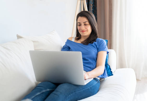 istock Happy smiling woman using a laptop computer while lying on sofa at home. Relaxing at home 1320639003
