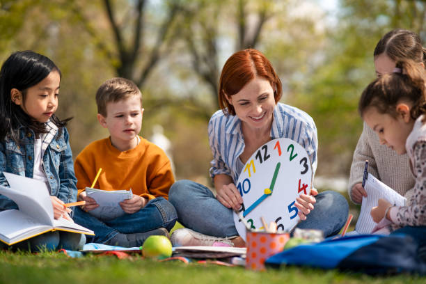 istock Teacher with small children sitting outdoors in city park, learning group education concept. 1320640093