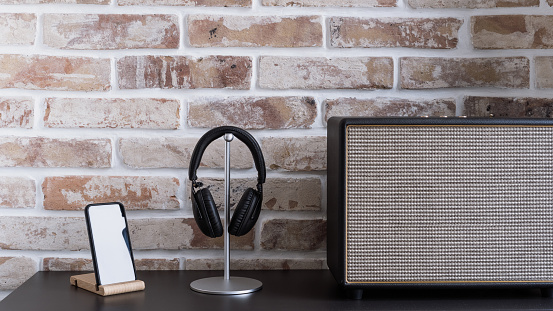 Audio equipment for home entertainment. Music column, smartphone mockup on wooden stand and headphones on table against brick wall