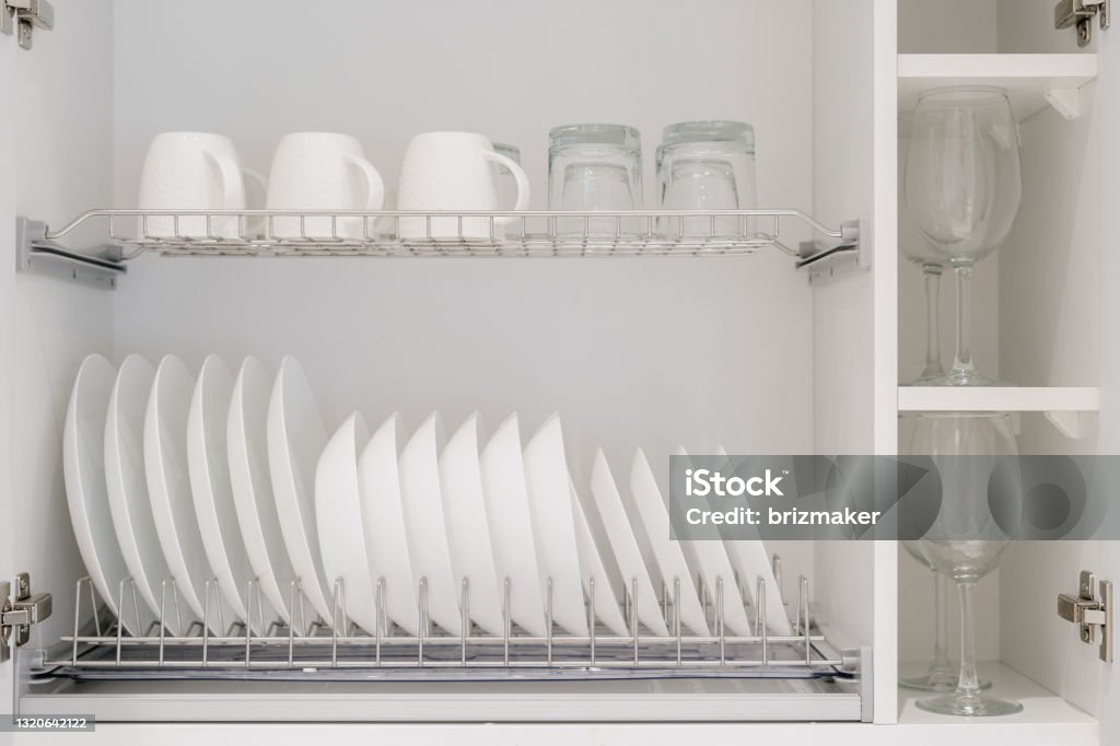 White kitchen storage cabinet with clean dishes Set of clean white dishes, mugs and different glasses and other crockery in opened white kitchen cupboard shelf. Close up of storage cabinet with kitchenware inside Cabinet Stock Photo